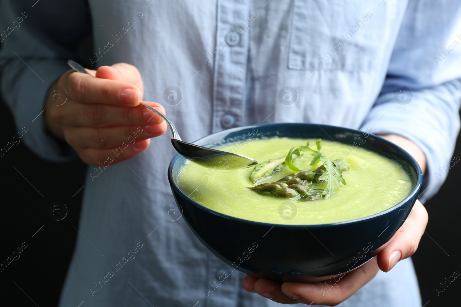 Photo of Woman eating delicious asparagus soup on black background, closeup