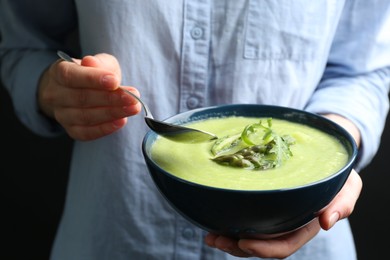 Photo of Woman eating delicious asparagus soup on black background, closeup