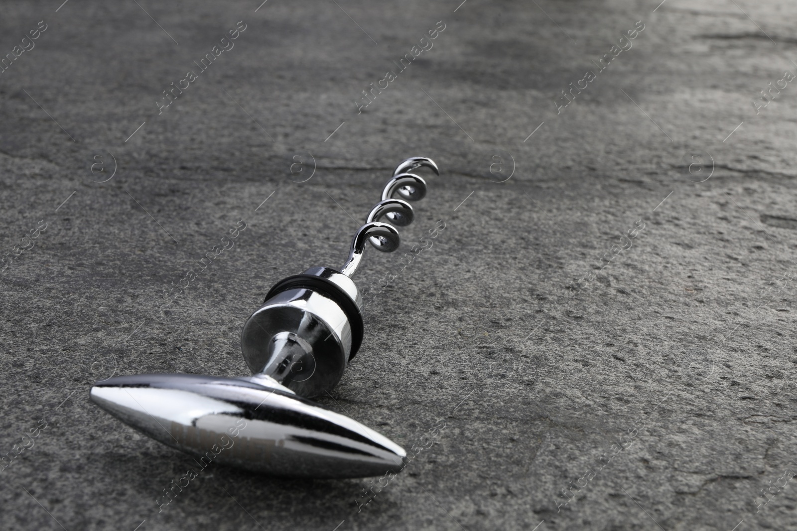 Photo of One metal corkscrew on grey textured table, closeup. Space for text