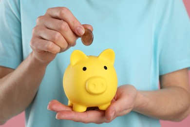 Photo of Woman putting coin into yellow piggy bank on pink background, closeup