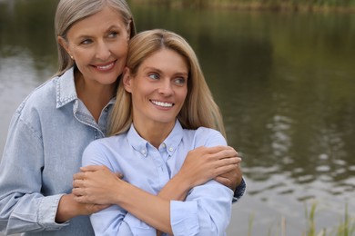 Photo of Happy mature mother and her daughter hugging near pond