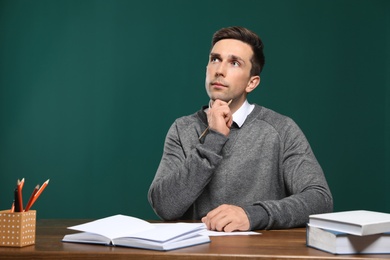 Portrait of male teacher working at table against color background