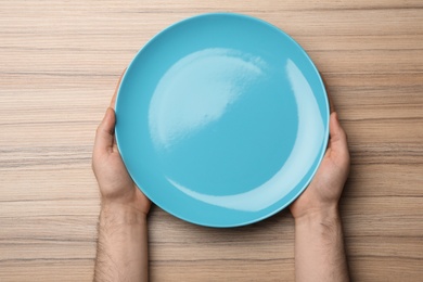 Man with empty plate at wooden table, top view