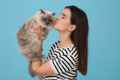 Photo of Woman kissing her cute cat on light blue background