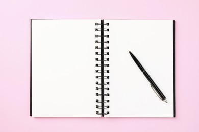 Photo of Notebook and pen on pale pink background, top view