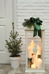 Beautiful Christmas lantern and potted fir tree near entrance indoors