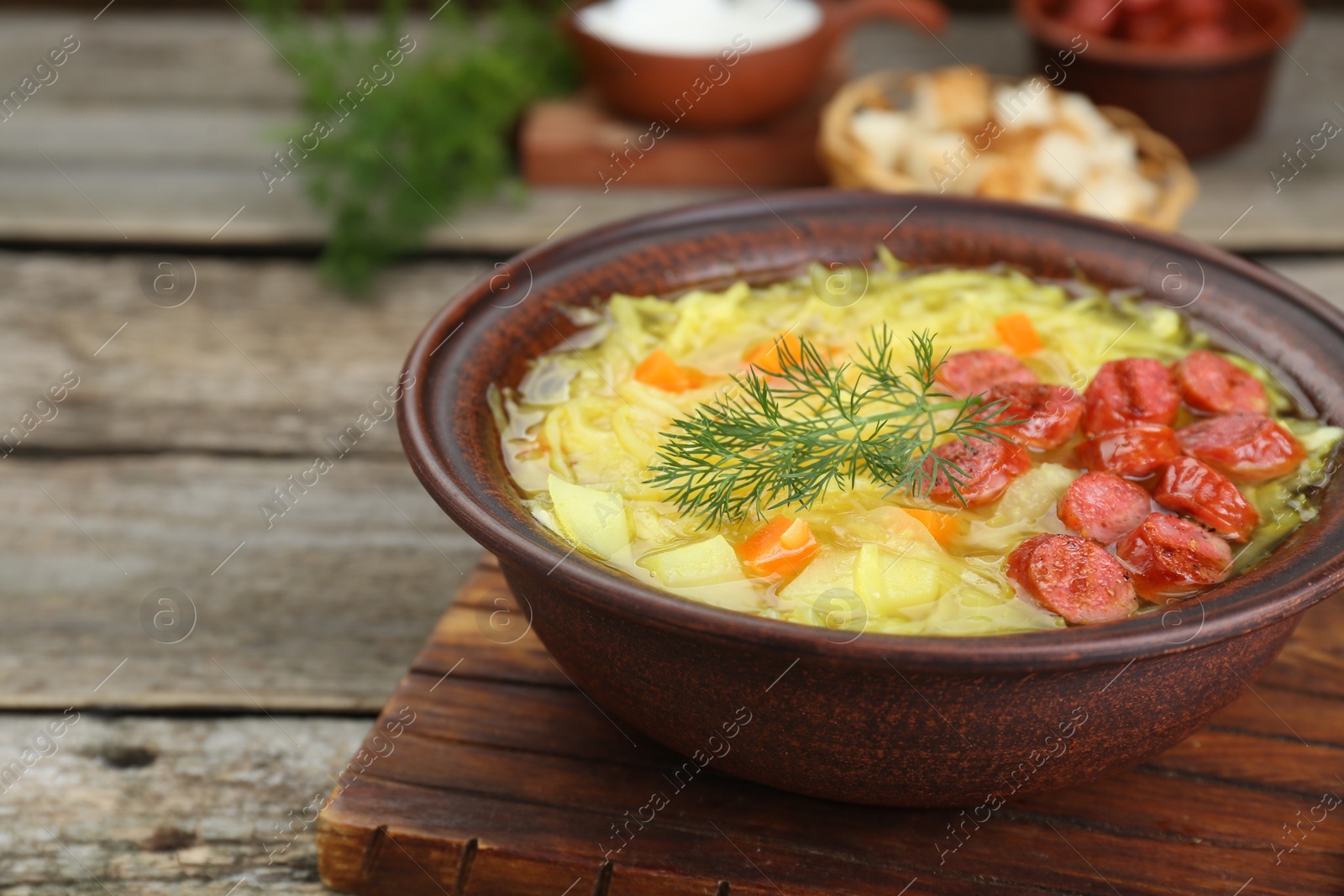 Photo of Bowl of delicious sauerkraut soup with smoked sausages and dill on wooden table, closeup