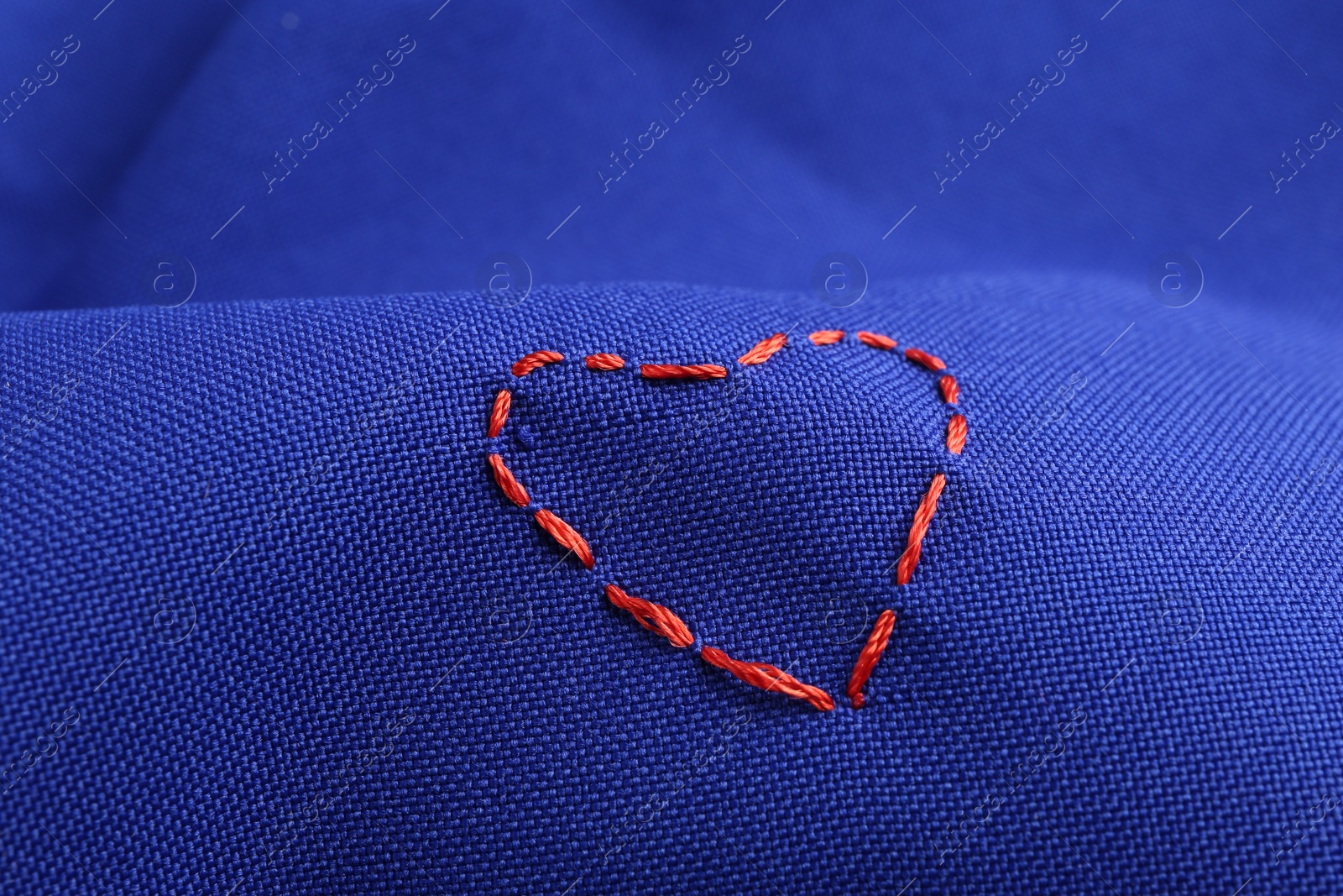 Photo of Red embroidered heart on blue cloth, closeup