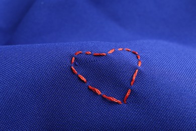 Photo of Red embroidered heart on blue cloth, closeup
