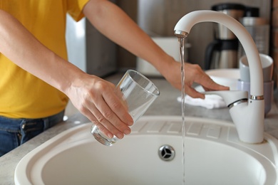 Photo of Woman filling glass with water from faucet in kitchen, closeup