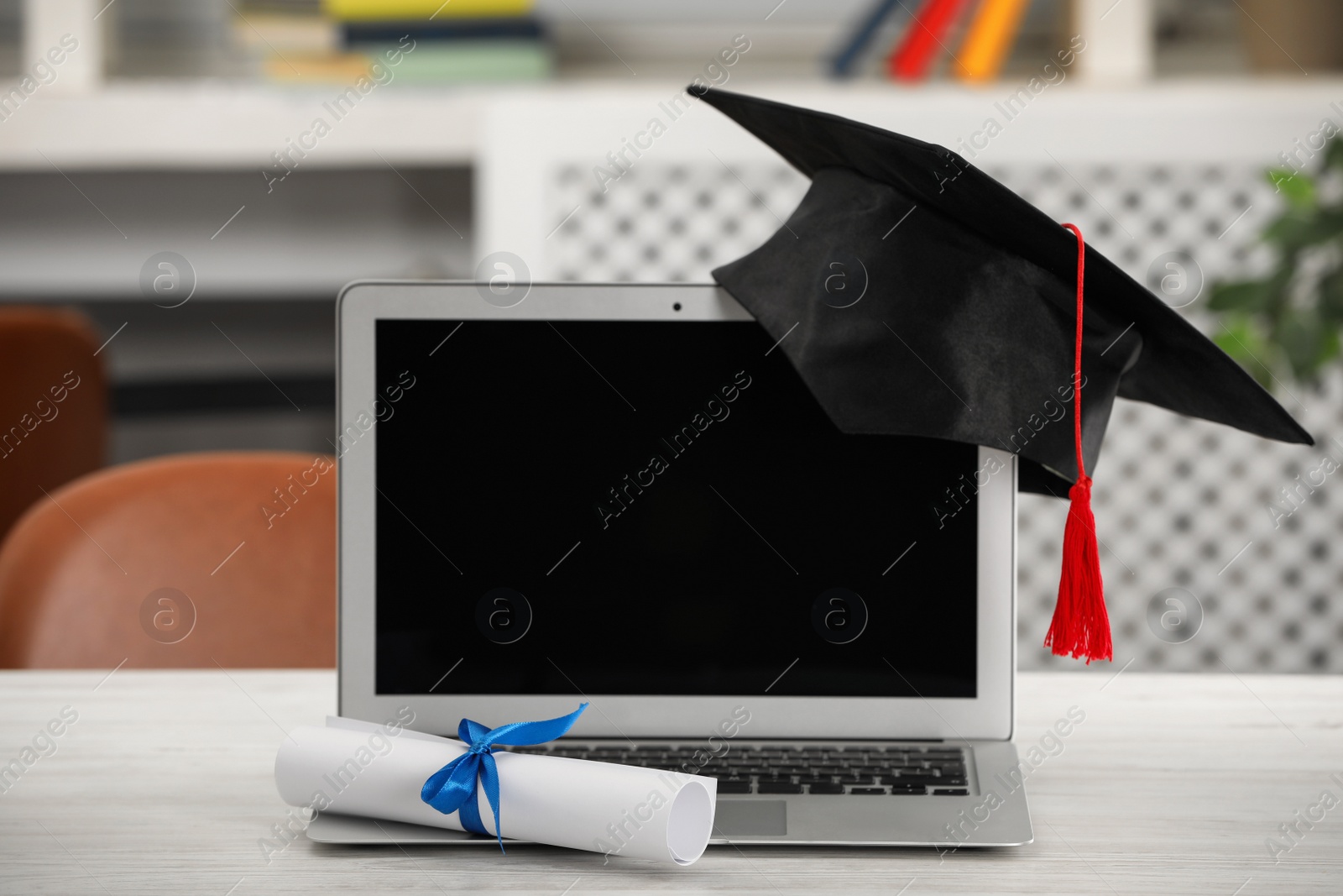 Photo of Graduation hat, student's diploma and laptop on white table indoors