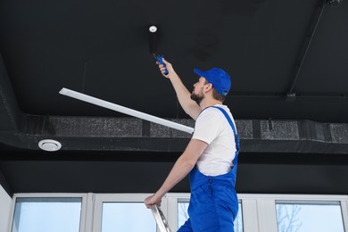 Worker in uniform painting ceiling with roller indoors