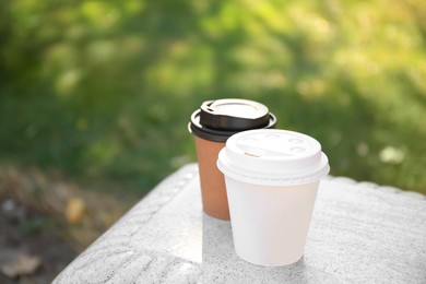 Cardboard cups with tasty coffee on stone bench outdoors. Space for text