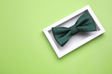 Photo of Stylish color bow tie with polka dot pattern in box on light green background, top view. Space for text
