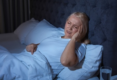 Mature woman suffering from headache in bed at night