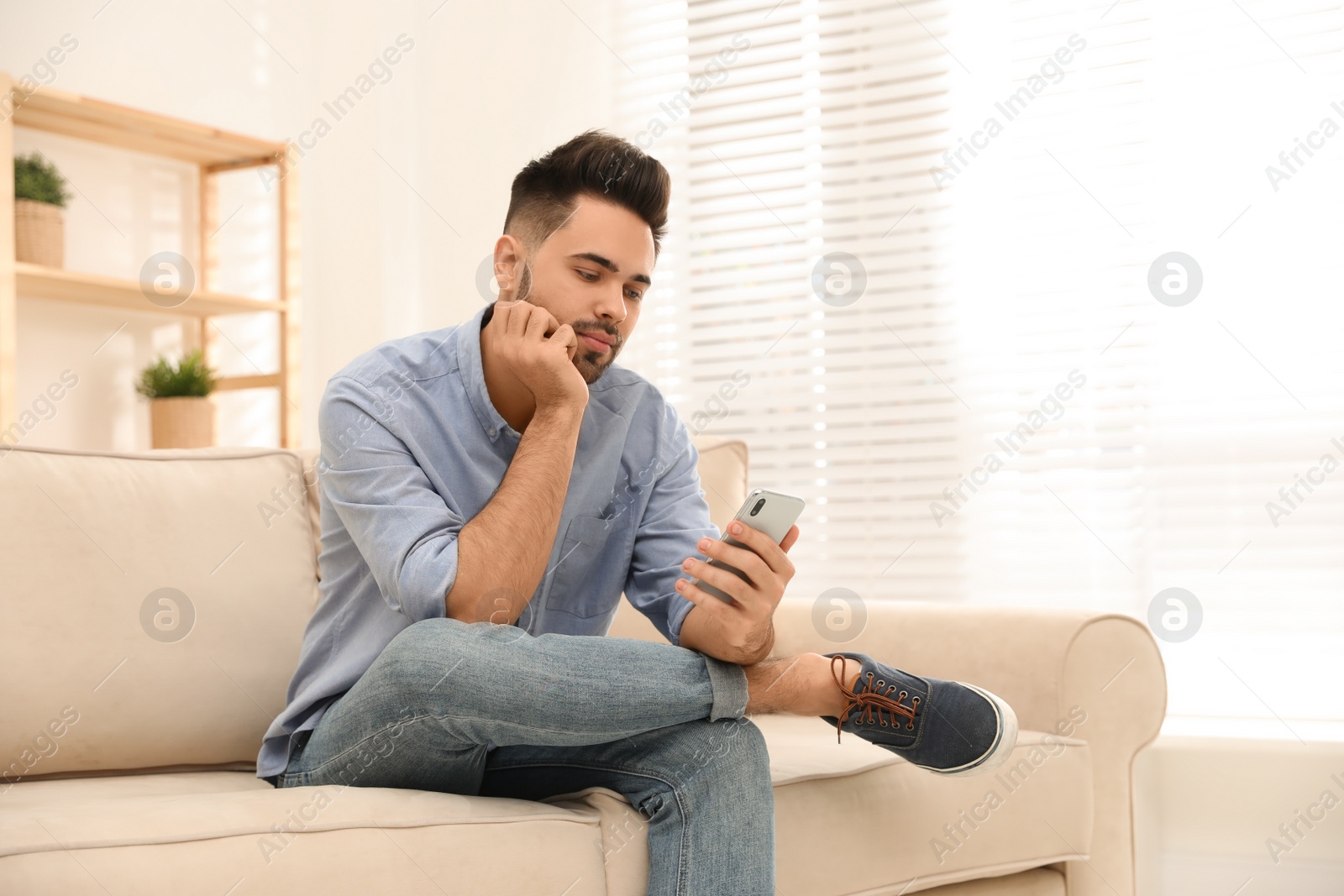 Photo of Young man addicted to smartphone on couch at home