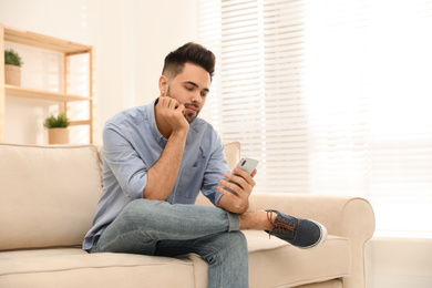 Young man addicted to smartphone on couch at home