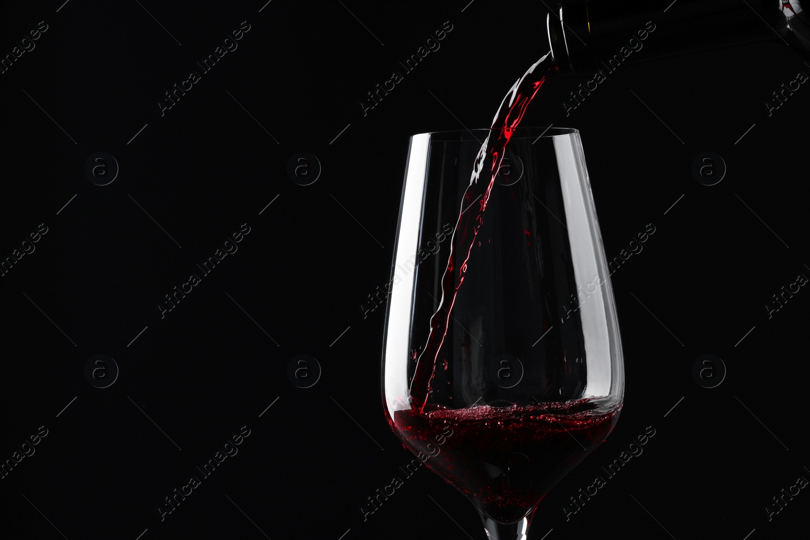 Photo of Pouring red wine into glass against black background, closeup. Space for text