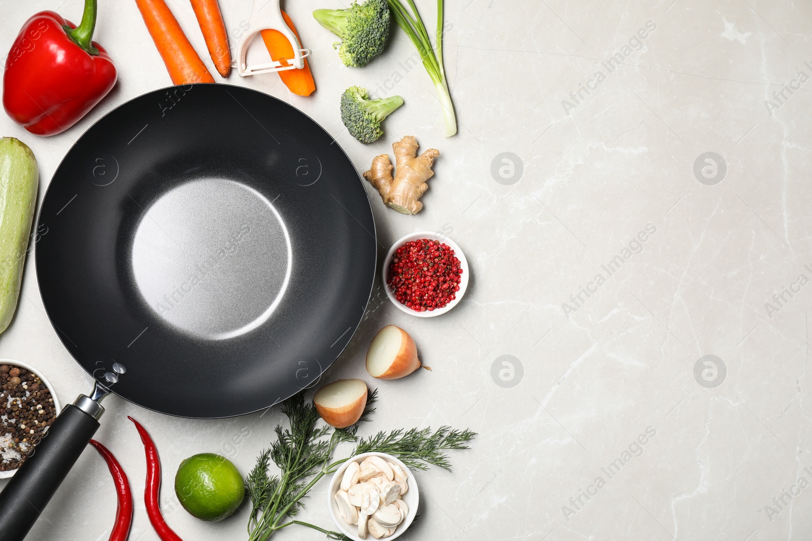 Photo of Empty iron wok surrounded by raw ingredients on light table, flat lay. Space for text