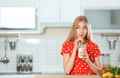 Photo of Young woman with glass of delicious milk shake in kitchen