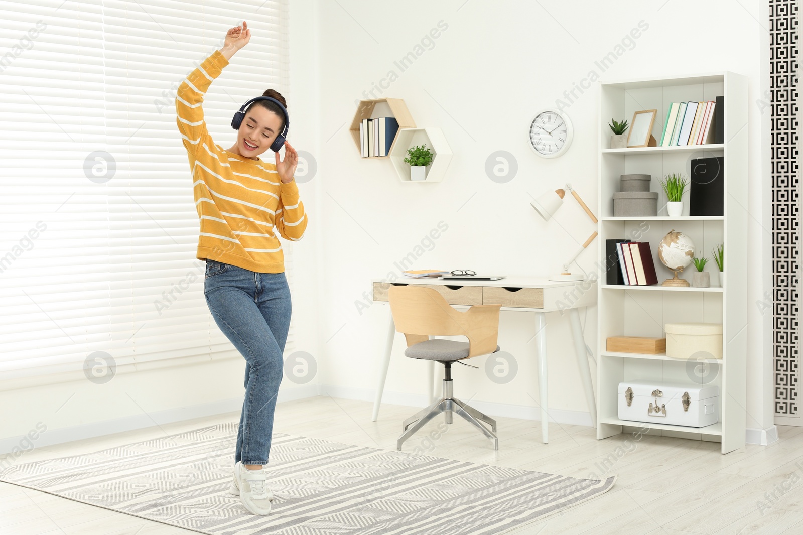 Photo of Happy woman in headphones listening music and dancing in cosy room