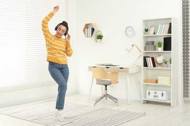 Photo of Happy woman in headphones listening music and dancing in cosy room