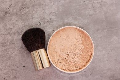 Face powder and brush on grey textured table, flat lay