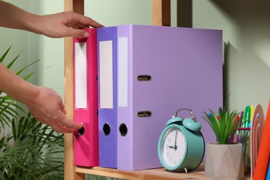 Photo of Woman taking binder office folder from shelving unit indoors, closeup