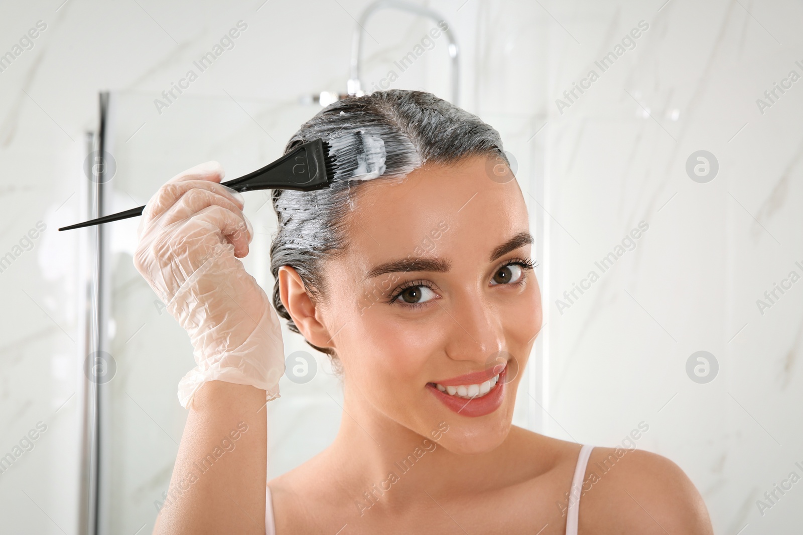 Photo of Young woman dyeing her hair in bathroom