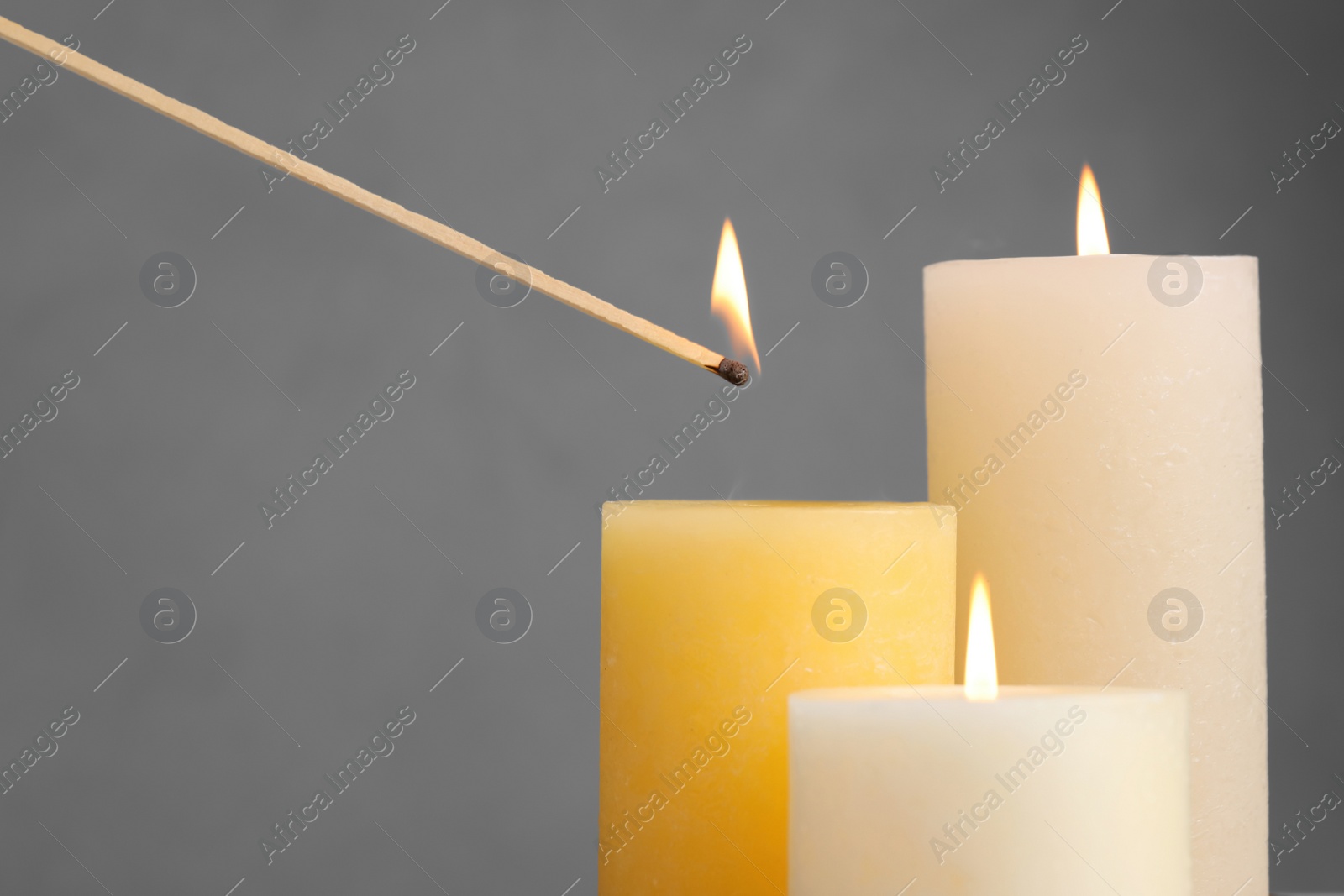 Photo of Lighting candle with wooden stick on grey background, closeup