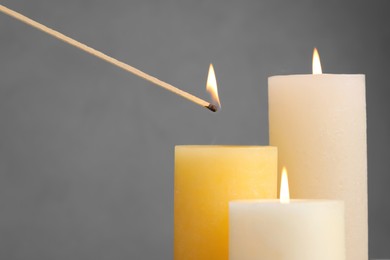 Photo of Lighting candle with wooden stick on grey background, closeup