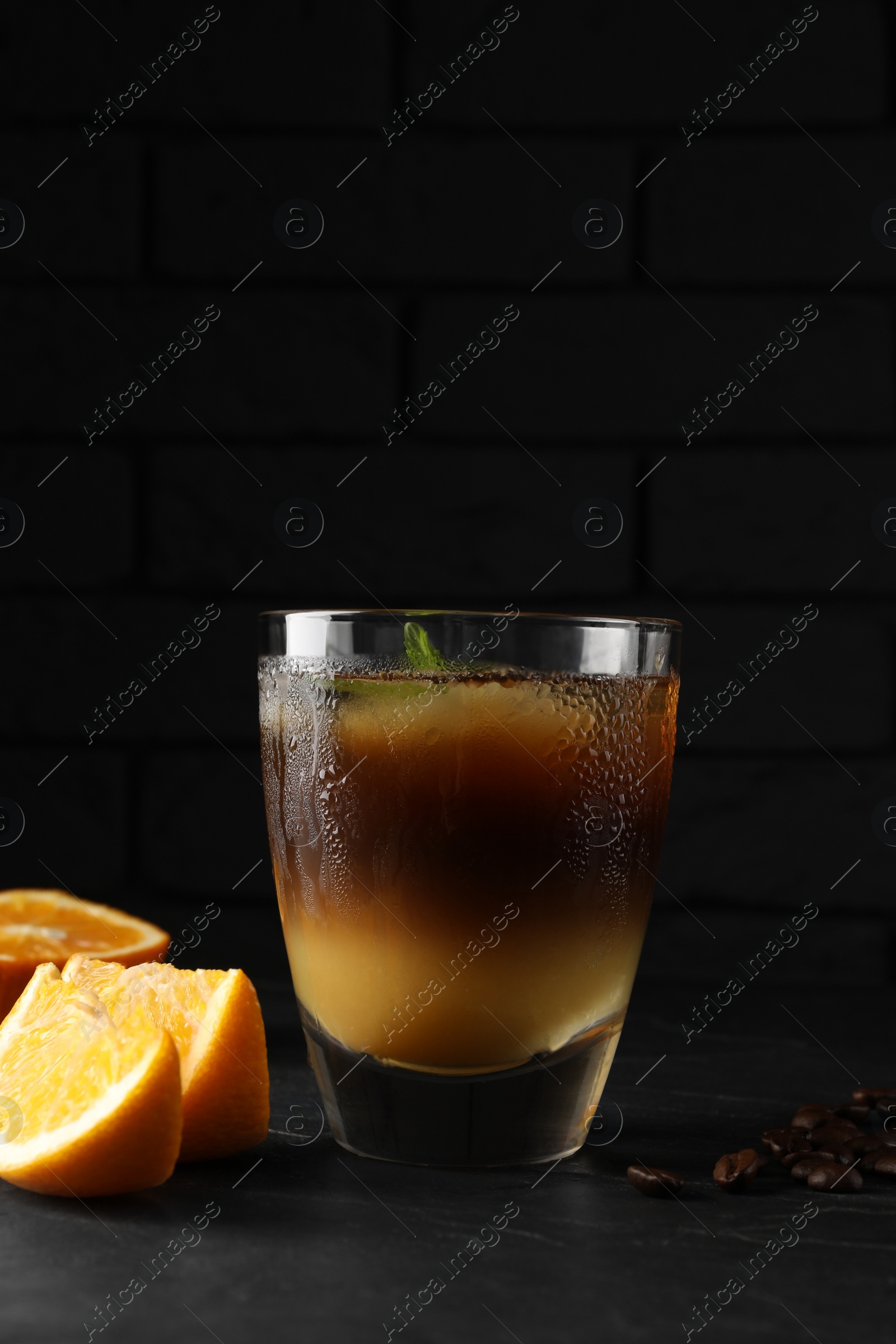 Photo of Tasty refreshing drink with coffee and orange juice on grey table against dark background