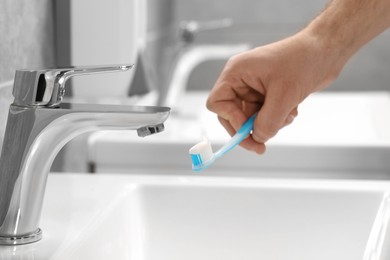 Photo of Man holding toothbrush with paste above sink in bathroom, closeup