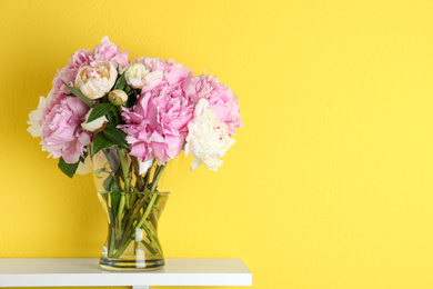 Photo of Beautiful peonies on white table against yellow background. Space for text