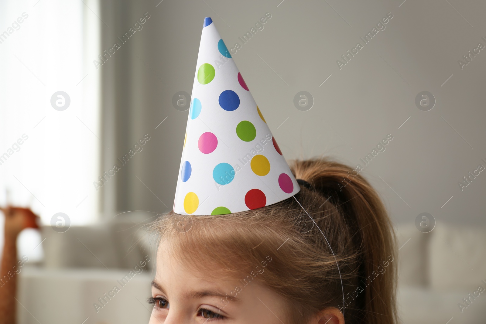 Photo of Cute little girl wearing party hat at home