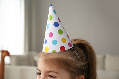 Cute little girl wearing party hat at home