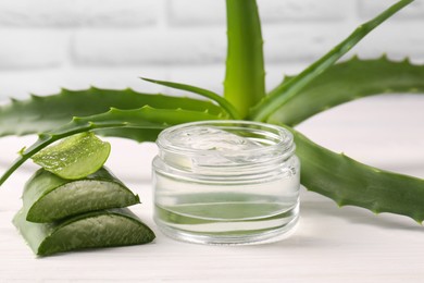 Photo of Jar of cosmetic gel and cut aloe vera leaves on white wooden table, closeup