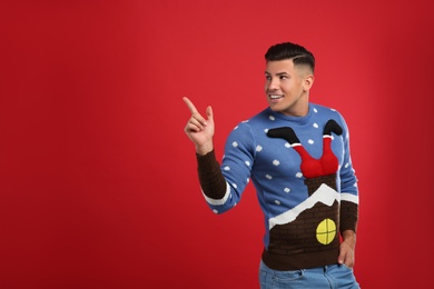 Happy man in Christmas sweater on red background, space for text