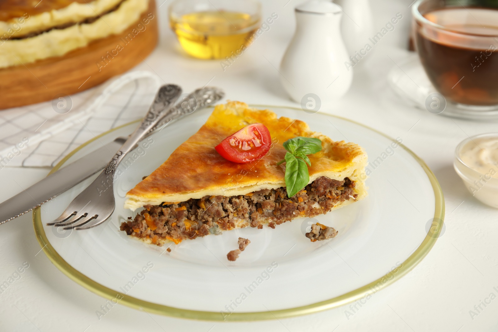 Photo of Piece of delicious pie with minced meat, tomato and basil served on white table, closeup