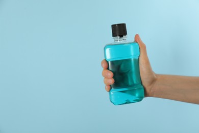 Photo of Woman holding bottle with mouthwash on light blue background, closeup. Space for text
