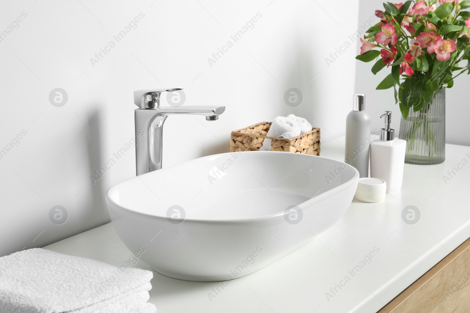 Photo of Vase with beautiful Alstroemeria flowers and toiletries near sink in bathroom