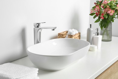 Vase with beautiful Alstroemeria flowers and toiletries near sink in bathroom