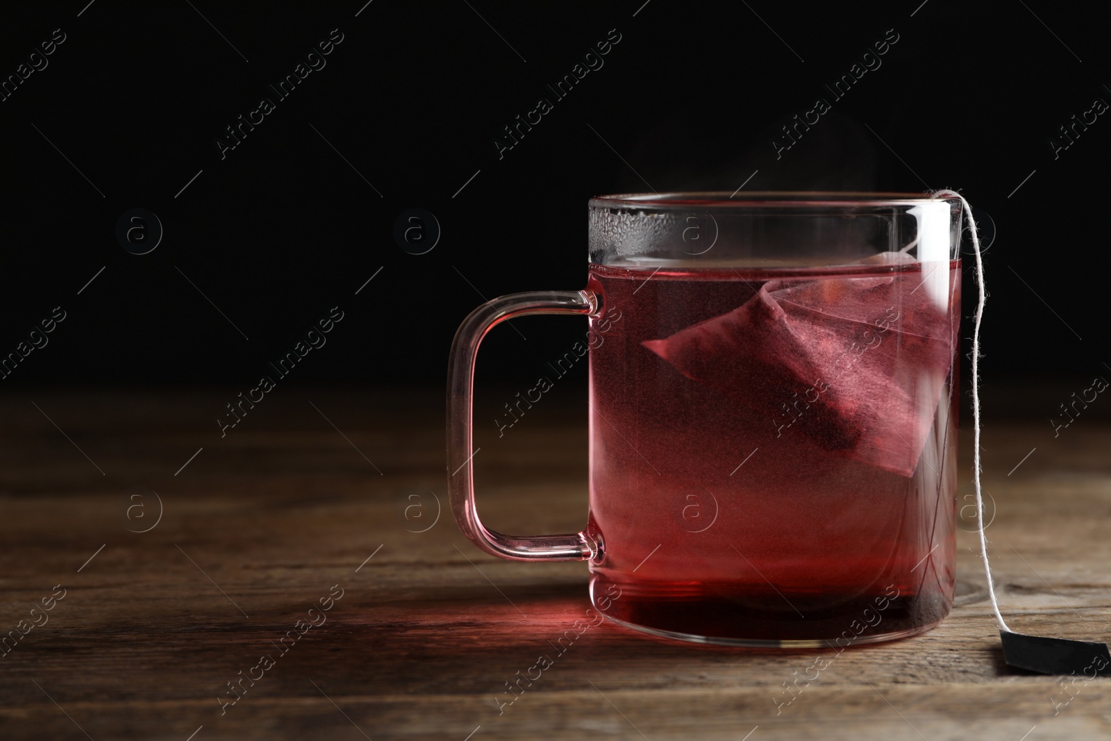 Photo of Tea bag in cup of hot water on wooden table. Space for text