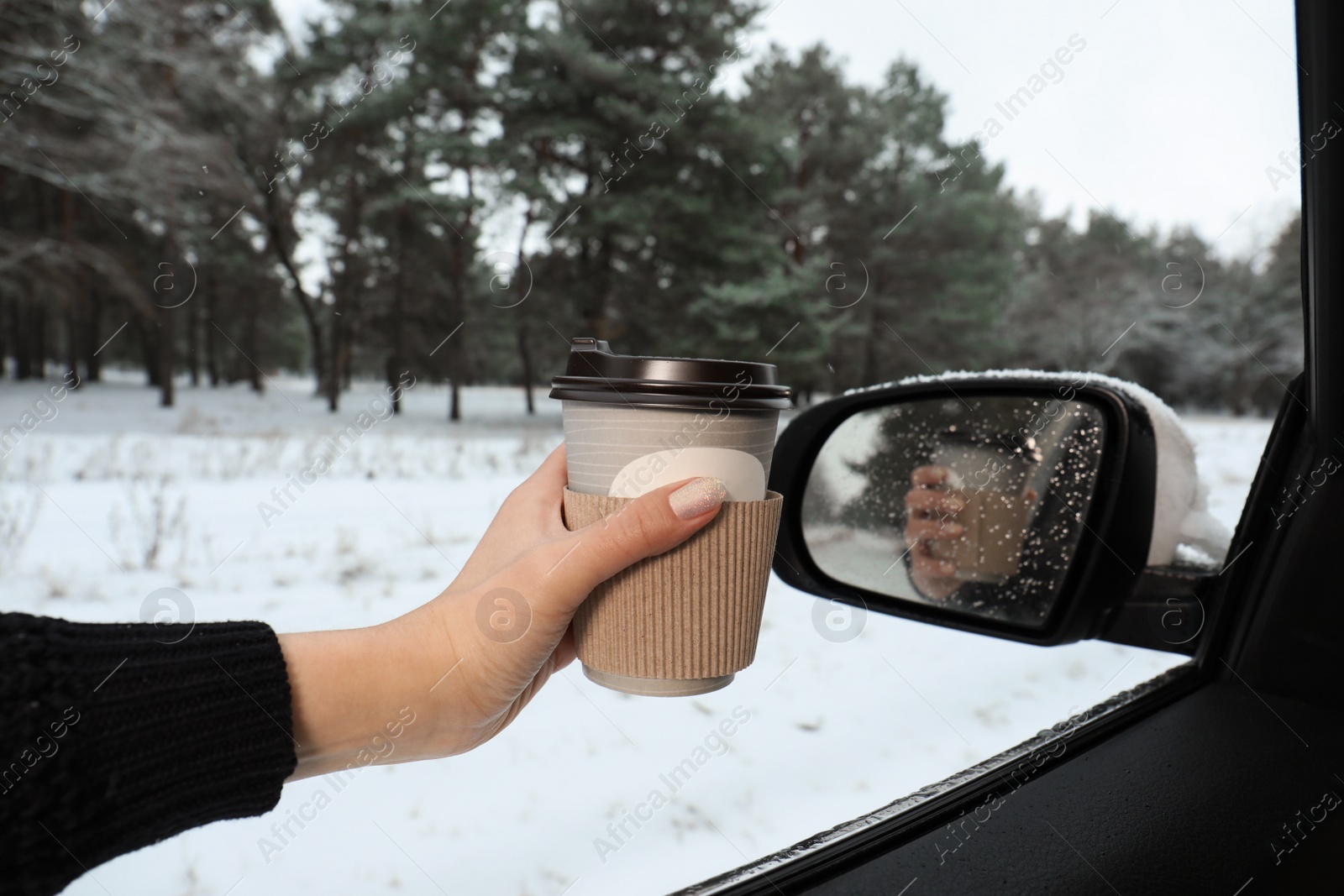 Photo of Young woman with coffee in car among winter forest, closeup