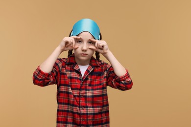 Girl with sleep mask on beige background, space for text. Insomnia problem