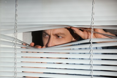 Curious man looking through Venetian window blinds