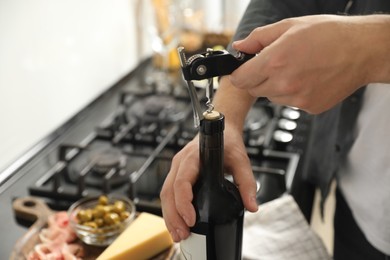 Man opening wine bottle with corkscrew indoors, closeup