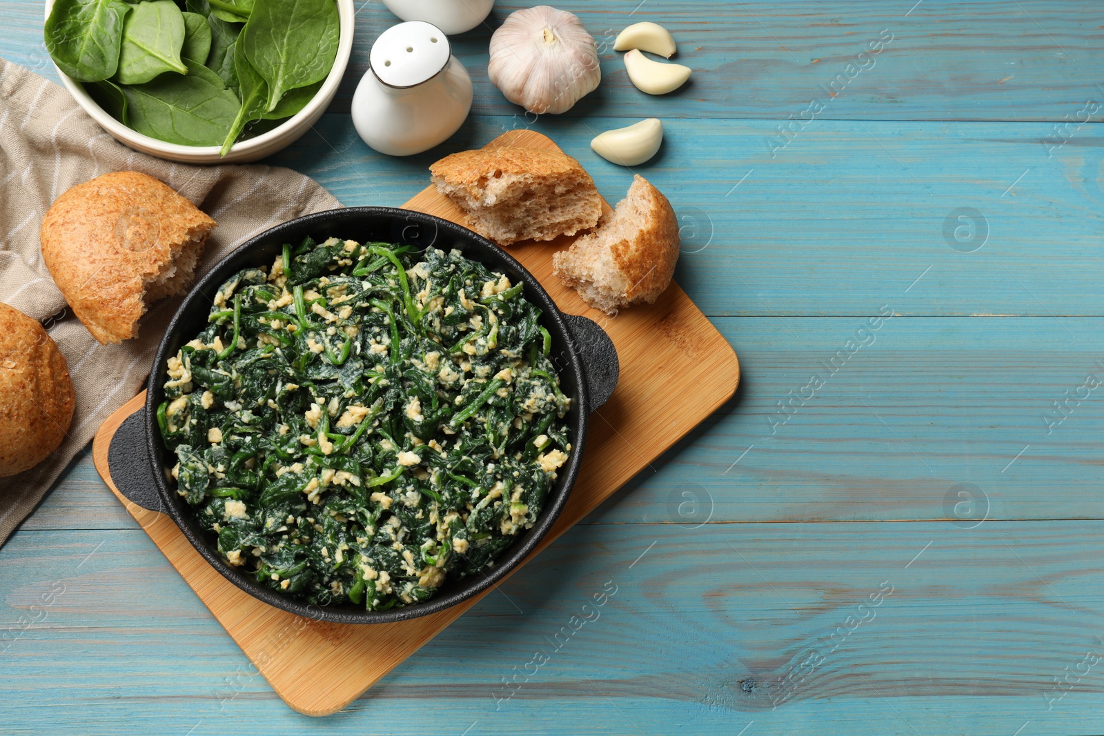 Photo of Tasty spinach dip with eggs in dish served on light blue wooden table, flat lay. Space for text