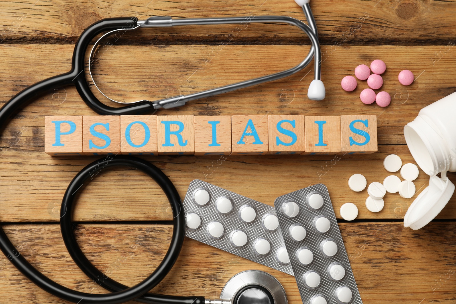 Photo of Word Psoriasis made of cubes with letters, stethoscope and pills on wooden table, flat lay