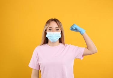 Woman with protective mask and gloves showing muscles on yellow background. Strong immunity concept